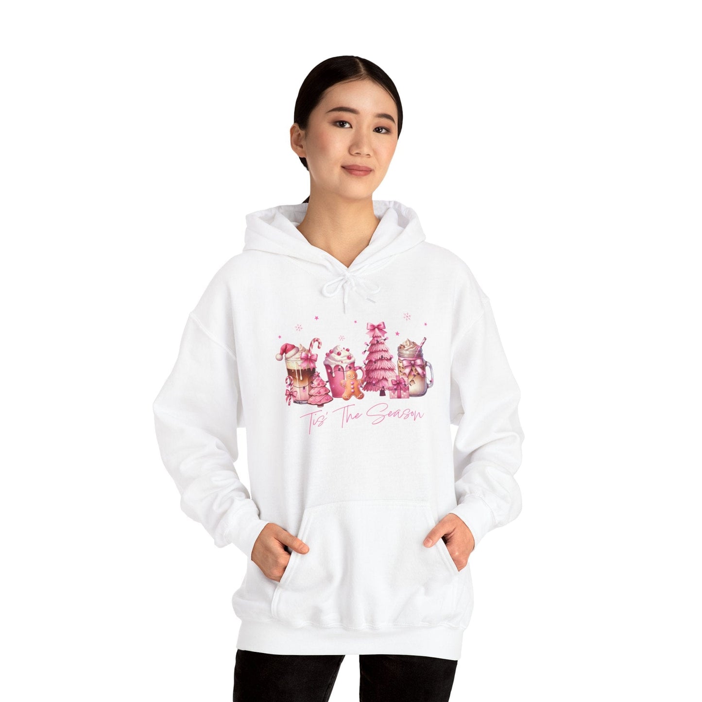 femaie model wearing hope + joy collective white hoodie sweatshirt with "Tis the Season" in cursive font below a graphic image of seasonal coffee and cocoa drinks accented in pink with a pink Christmas tree topped with pink bow