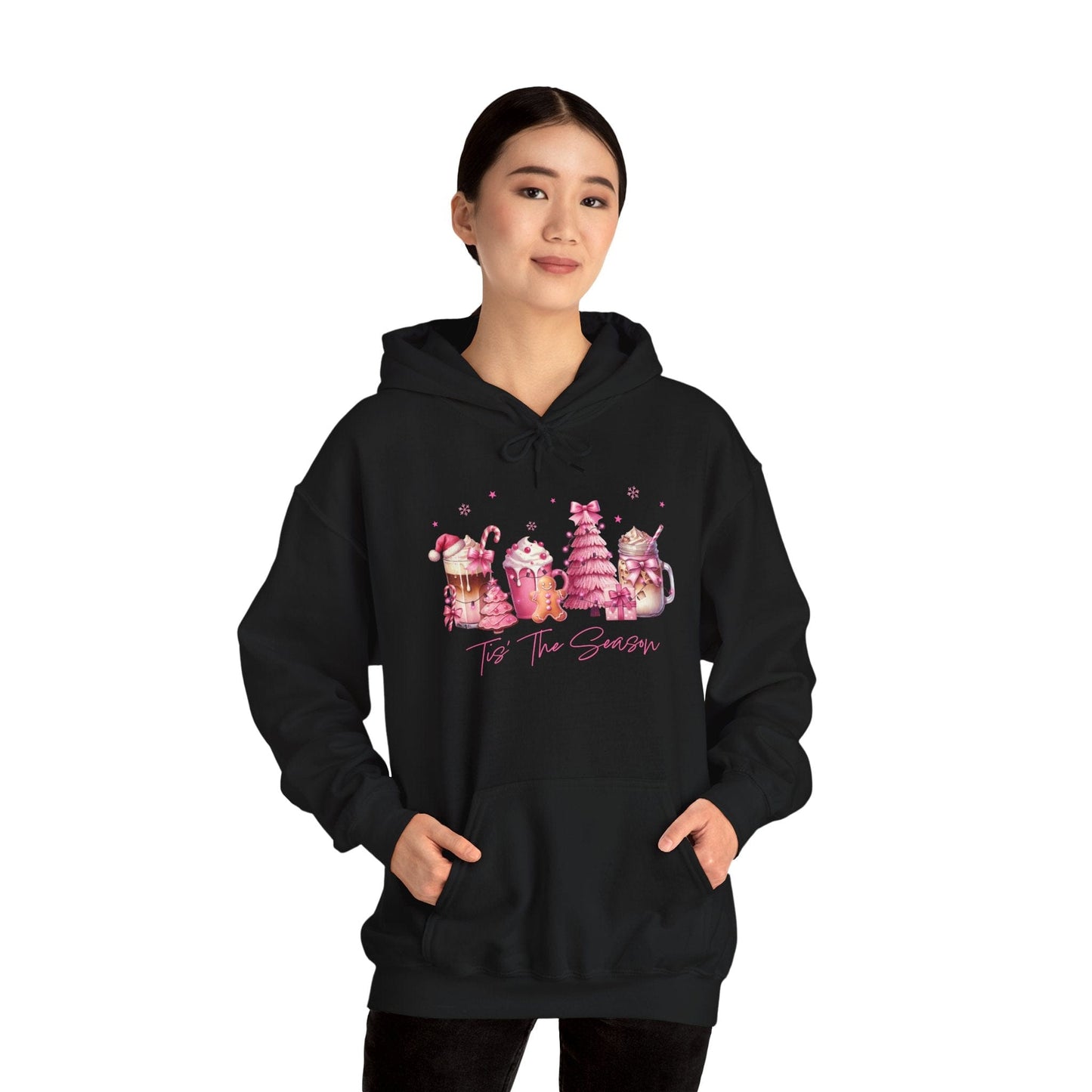 female model wearing hope + joy collective black hoodie sweatshirt with "Tis the Season" in cursive font below a graphic image of seasonal coffee and cocoa drinks accented in pink with a pink Christmas tree topped with pink bow