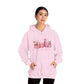 femaie model wearing hope + joy collective pink hoodie sweatshirt with "Tis the Season" in cursive font below a graphic image of seasonal coffee and cocoa drinks accented in pink with a pink Christmas tree topped with pink bow
