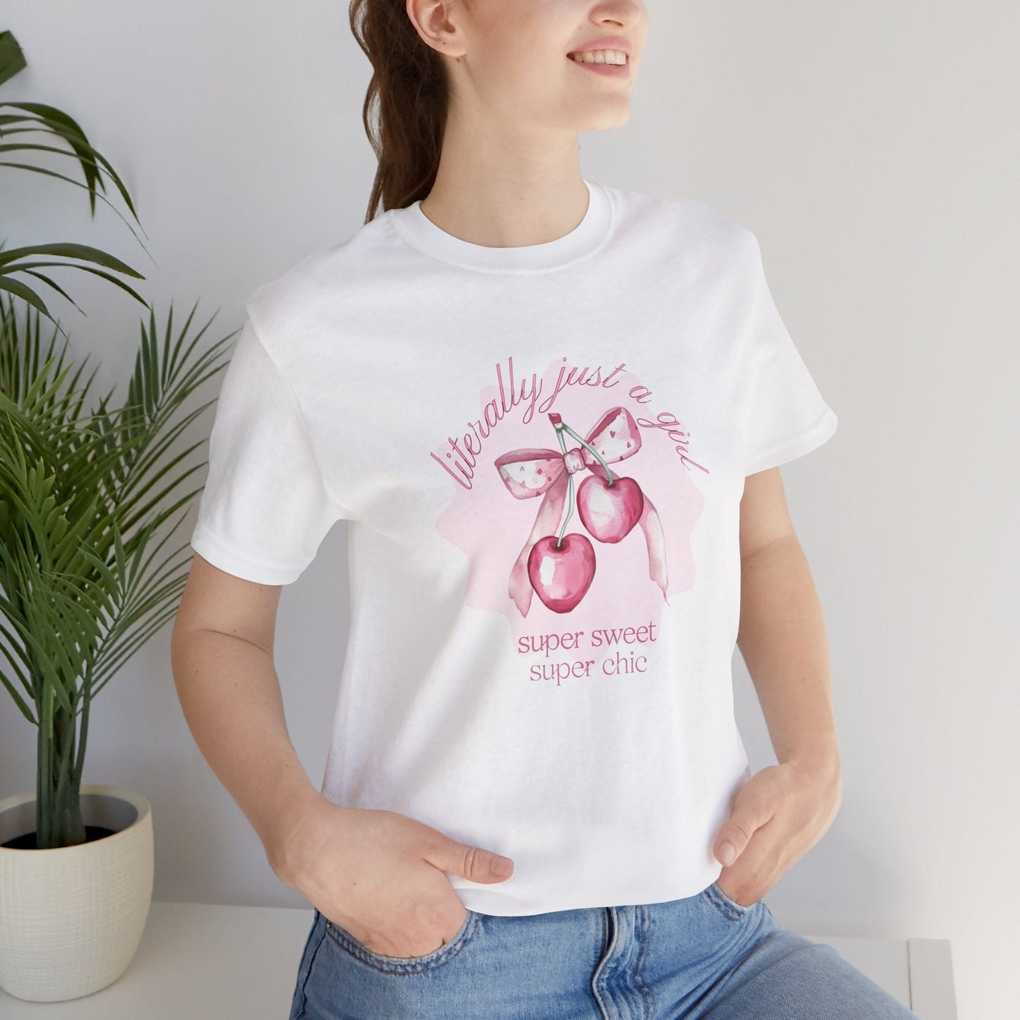 female model in jeans wearing hope + joy collective white short sleeve t-shirt with image of pink cherries with pink bow that says "literally just a girl, super sweet, super chic"