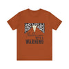 hope + joy collective autumn
 short sleeve t-shirt with a graphic image of a leopard banner and cow skull in the middle that says "Should've Come with a Warning" in western font