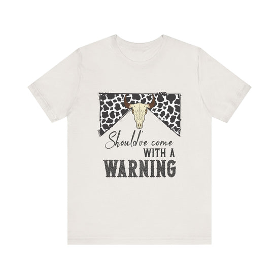 hope + joy collective heather vintage white short sleeve t-shirt with a graphic image of a leopard banner and cow skull in the middle that says "Should've Come with a Warning" in western font