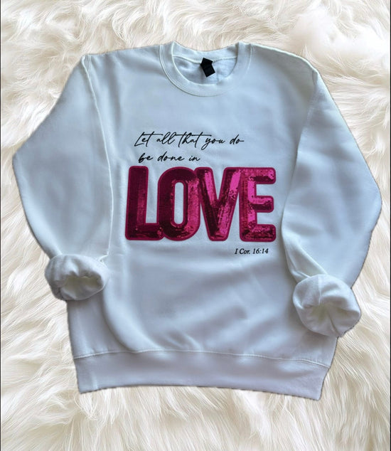 hope + joy collective Do All Things in Love Crewneck white crewneck sweatshirt with "Let all that you do be done in love" 1 Cor 16:14 in black cursive font, and "LOVE" is large bright pink sequin letters.